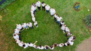 Menschen stehen in Herzform auf einer Wiese
