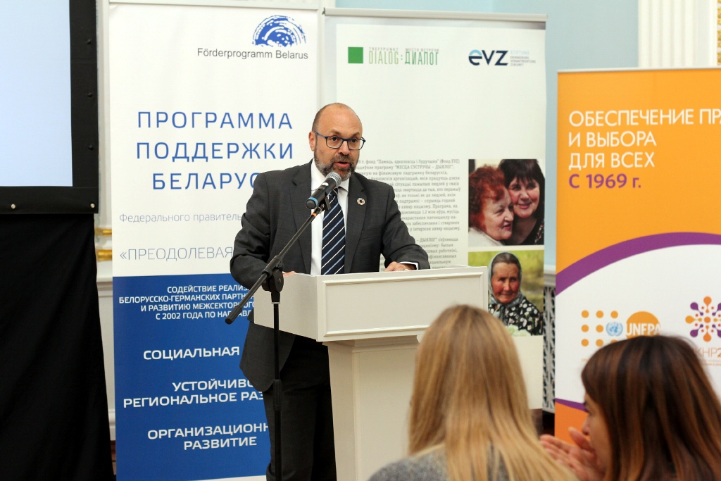 Jaime Nadal, Repräsentant des UNFPA, bei seiner Ansprache in Minsk am Rednerpult vor einem Aufsteller Förderprogramm Belarus.