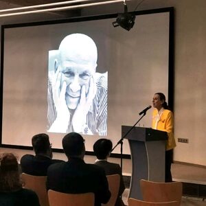 Galina Lewina am Rednerpult neben dem Portrait ihres warmherzig lächelnden Vaters.