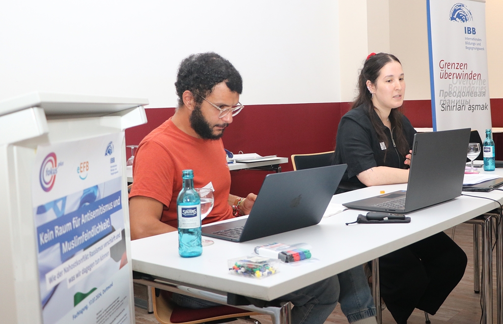 Polina Khubebeeva, rechts im Bild, und Iskandar Abdalla vom Projekt „Build Bridges, Not Barriers“ des Berliner Vereins Transaidency sitzen hinter aufgeklappten Laptops und berichten über ihre Arbeit mit Jugendlichen. 