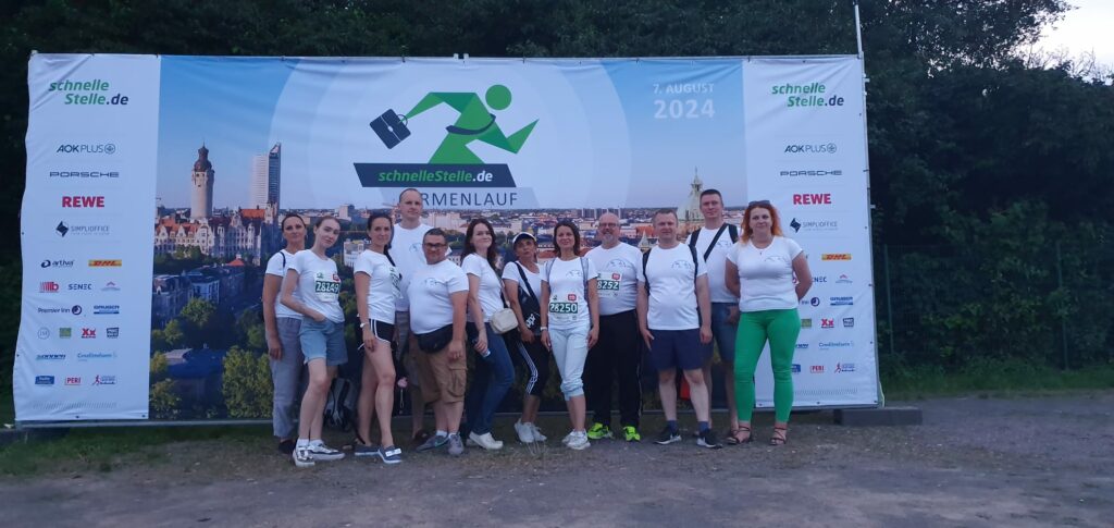 Unser Foto zeigt Mitarbeiterinnen und Mitarbeiter der IBB gGmbH Dortmund und der IBB "Johannes Rau" Minsk vor einem mehrere Meter hohen Plakat, das für den Leipziger Firmenlauf wirbt. 