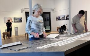 Ein Blick in die Ausstellung im Stadthaus: Mehrere Projektteilnehmende schauen intensiv auf die Texttafeln. An den Wänden hängen großformatige Fotos.