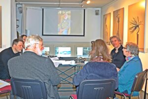 Blick auf eine Gesprächsrunde vor einem Beamer, auf dem ein Video des Zeitzeugen Kurt Marx abgespielt wird. 