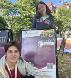 Mina vor dem Plakat für das Projekt „Das Erinnerungs-DING“ auf dem Gelände des Junify - Demokratiefestivals.